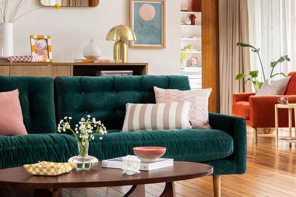 A Habitat green velvet sofa with a 3 pink cushions behind a walnut coffee table.